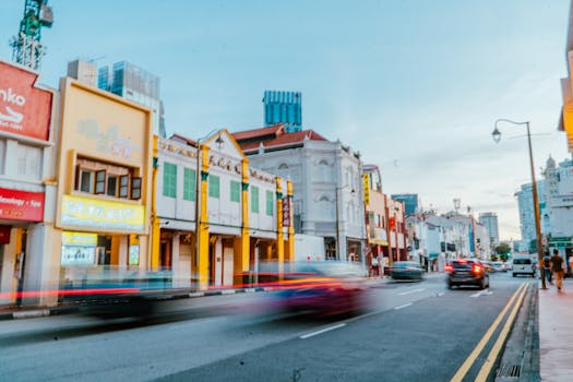 Chinatown street scene featuring colorful architecture and motion blur of passing cars at dusk.