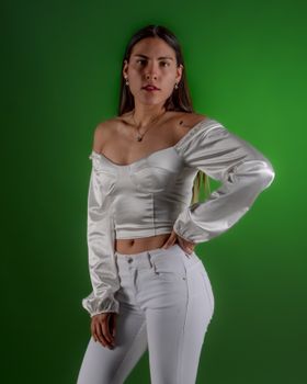Stylish young woman posing confidently in white top and pants against a vibrant green background.