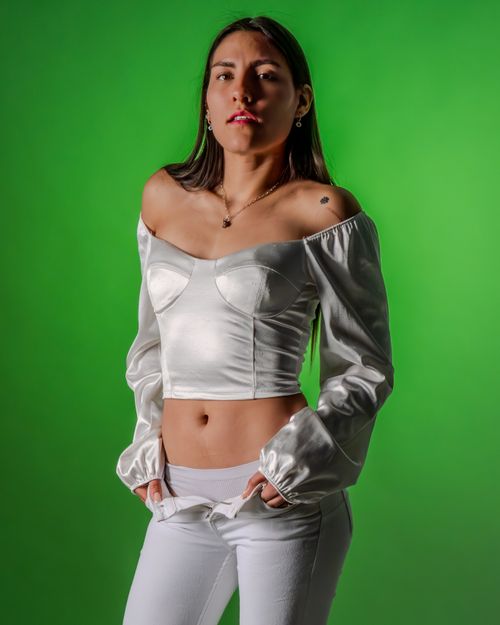 Free Confident woman posing in fashionable white attire against a vibrant green backdrop. Stock Photo
