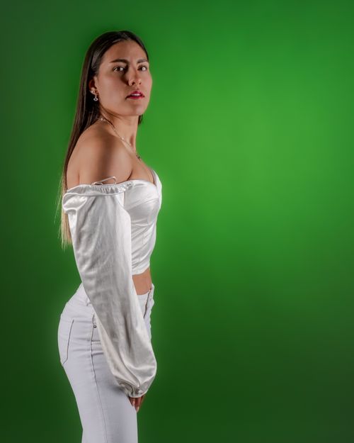Free Portrait of a stylish woman in white clothing posing against a vibrant green background. Stock Photo
