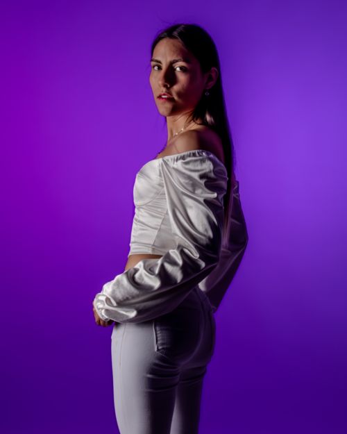 Free Elegant portrait of a stylish woman in white clothing against a vibrant purple backdrop. Stock Photo