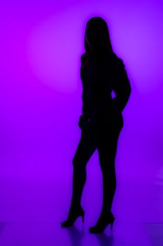 Silhouette of a woman in high heels standing against a vivid purple background, exuding confidence and style.