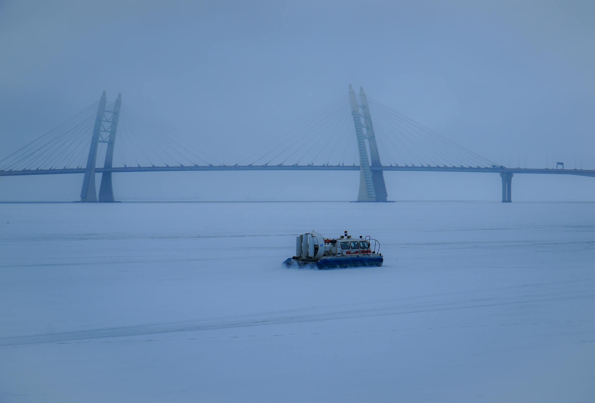 Hovercraft travels on frozen river beneath bridge in Saint Petersburg.
