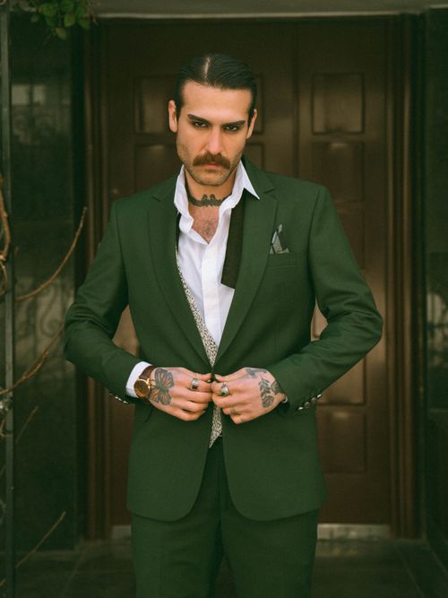 Free Confident man in green suit adjusting tie, showing tattoos. Stock Photo