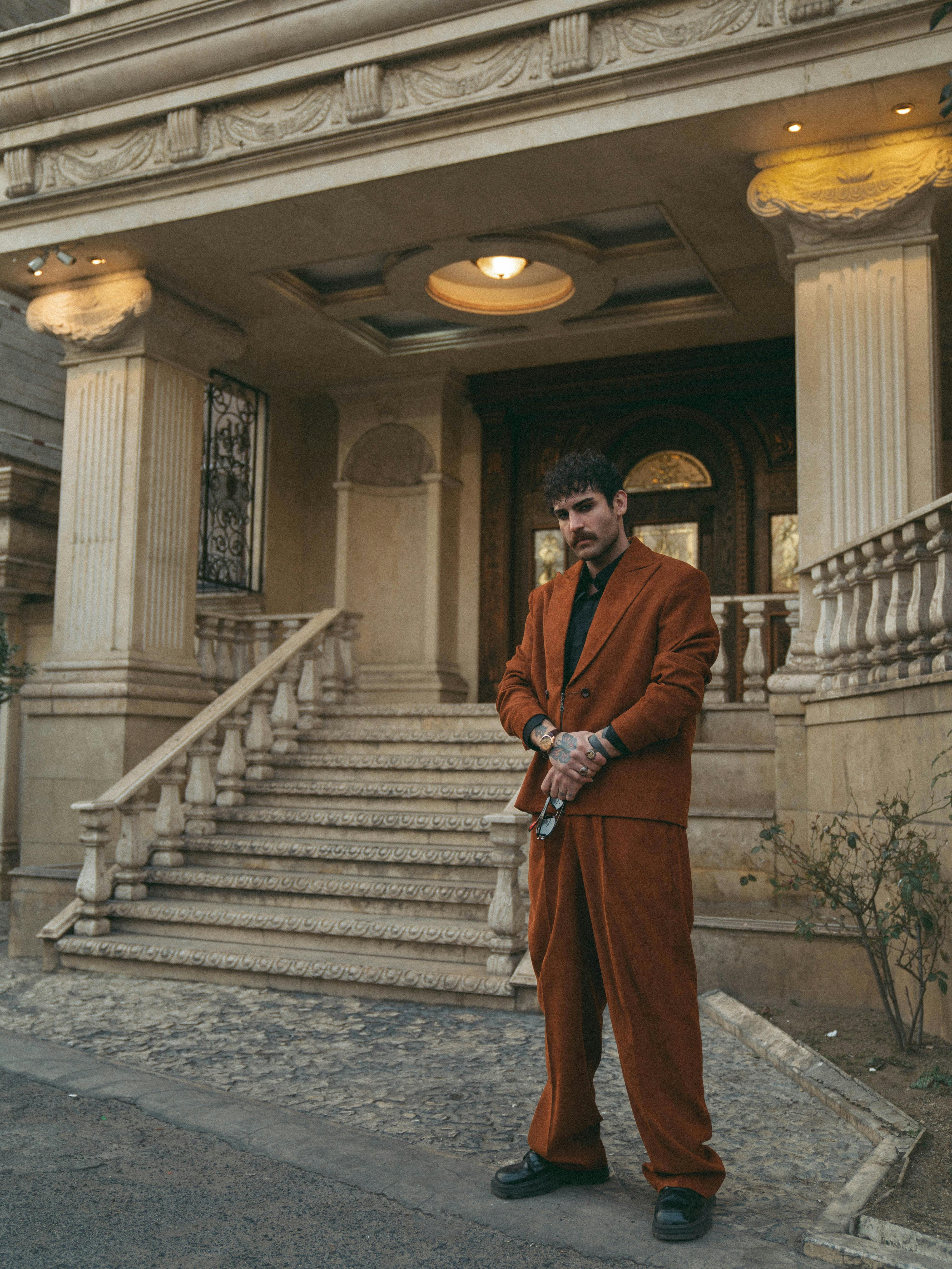 Man in vintage-style suit poses confidently at a grand entrance, evoking a cinematic vibe.