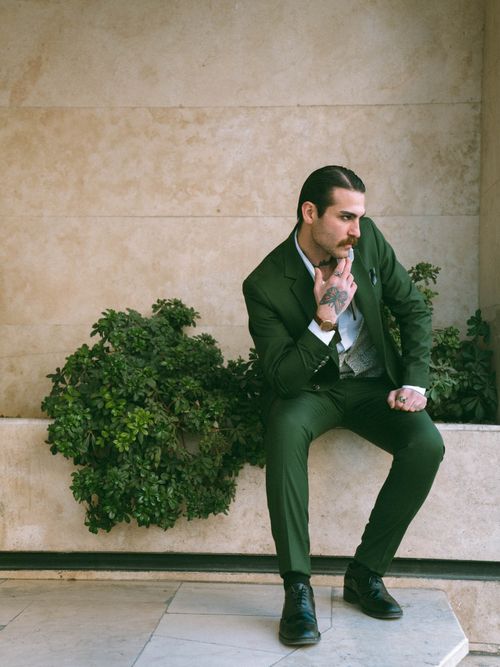 Free Man in a green suit sitting indoors, exuding confidence with a thoughtful pose. Stock Photo