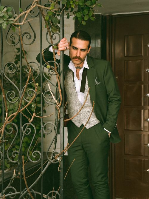 Free Sophisticated man in green suit leaning on ornate iron gate with a contemplative expression. Stock Photo