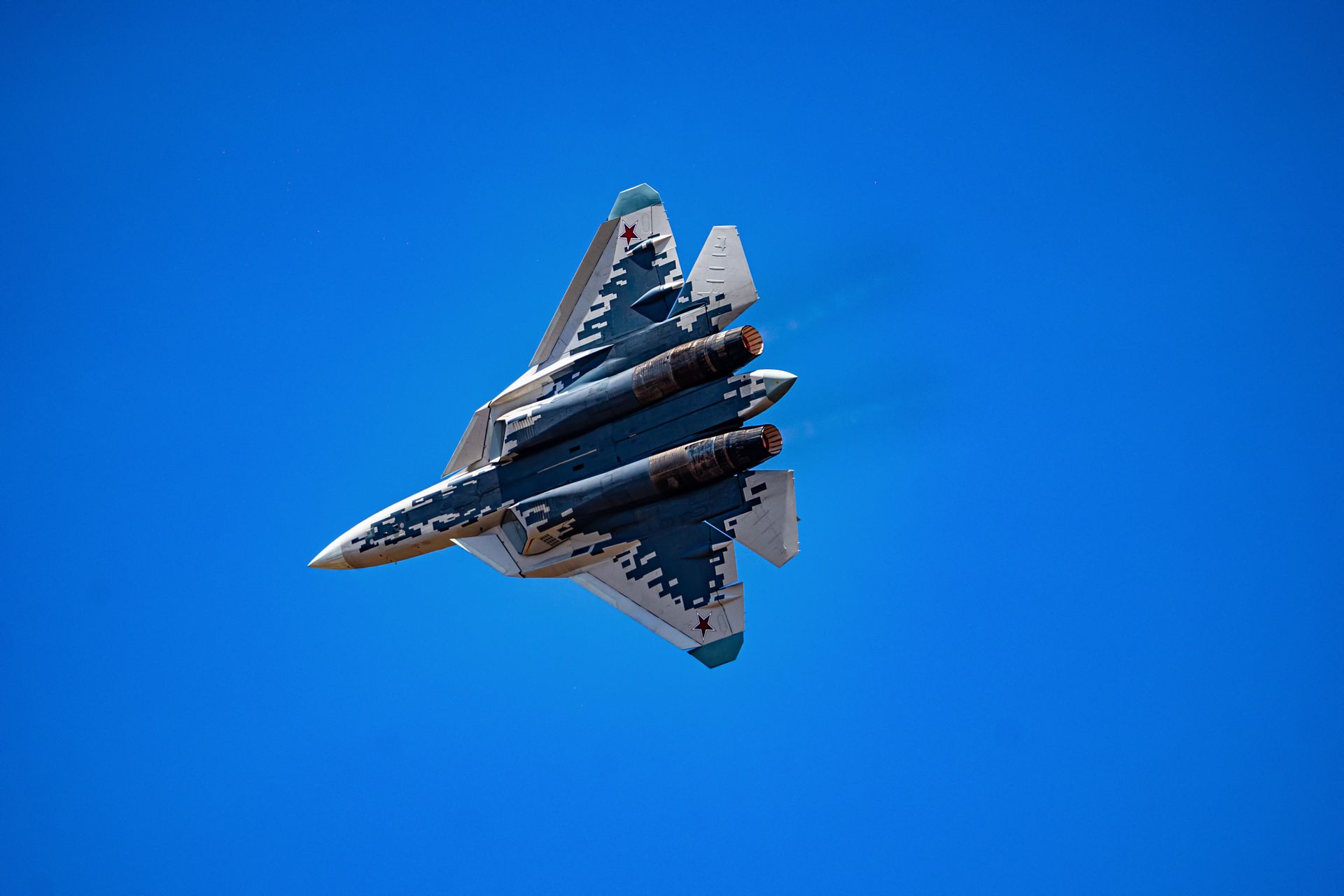 A military jet soars through a clear blue sky, showcasing agile maneuvers.