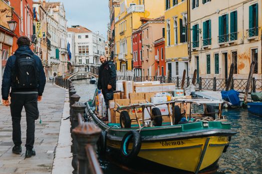 A canal boat loaded with goods navigates the colorful streets of Venice, Italy.