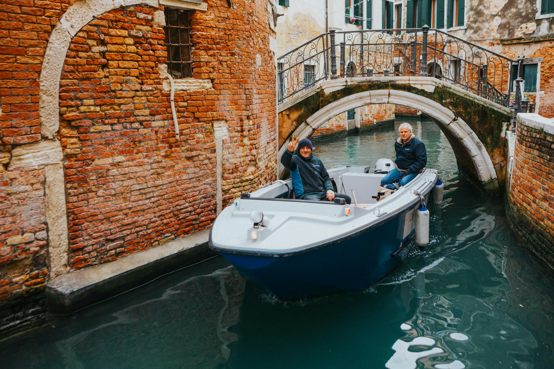 Tourists cruising through historic Venetian canals in a blue boat under a charming bridge.