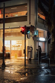 Rainy street in Kuzguncuk, Istanbul with illuminated storefront and traffic lights at night.