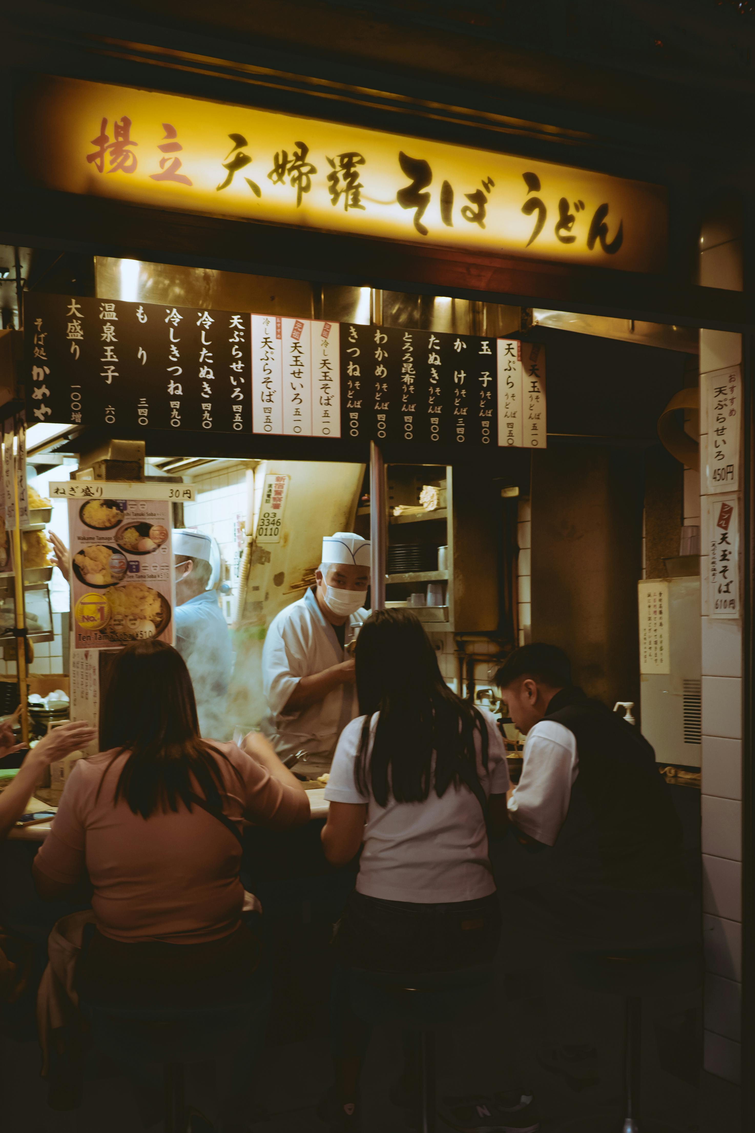 Customers enjoy soba noodles at a traditional udon shop in Japan, captured during a busy evening.