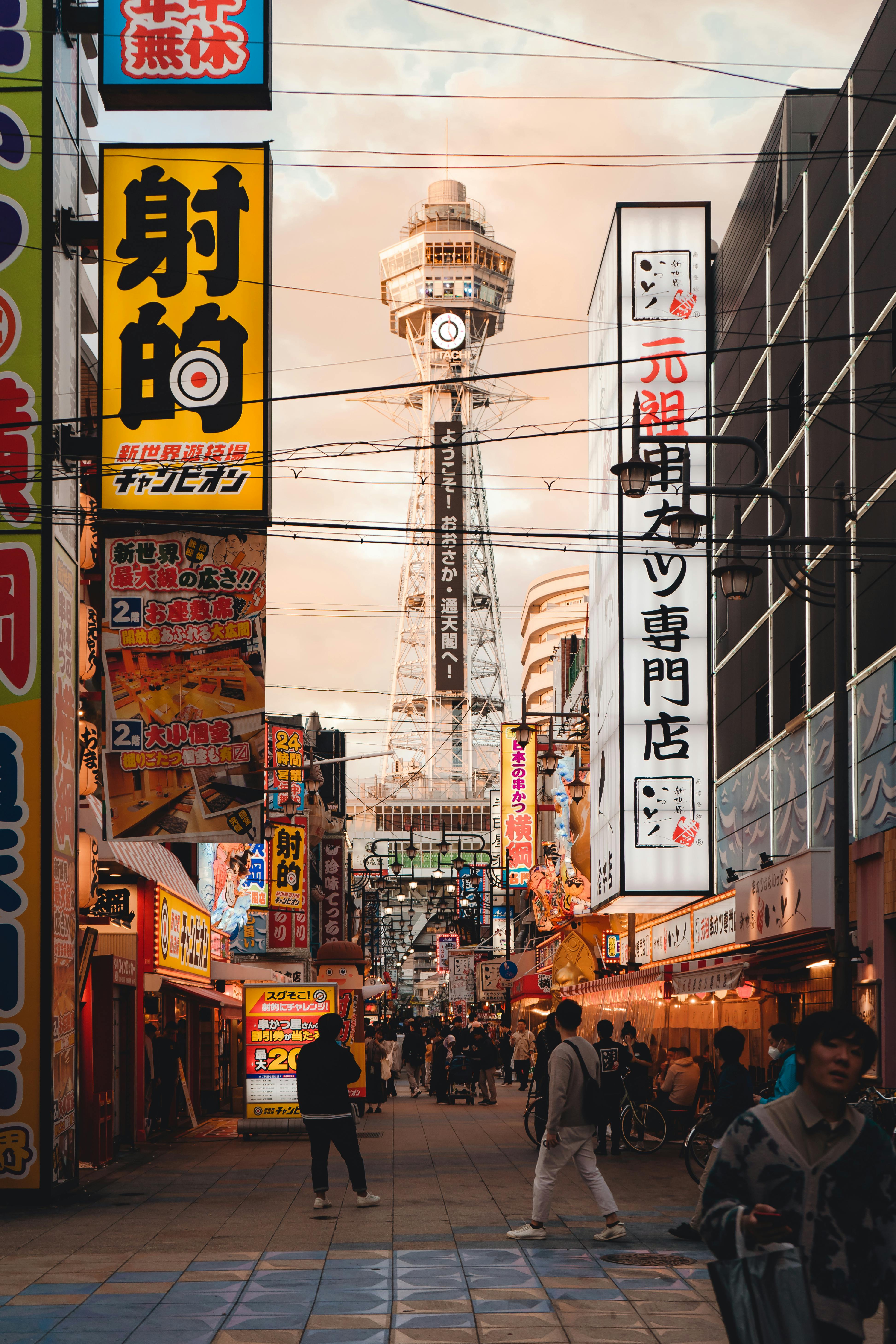 Lively street scene in Osaka featuring Tsutenkaku Tower with vibrant signs and bustling crowds.