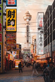 Lively street scene in Osaka featuring Tsutenkaku Tower with vibrant signs and bustling crowds.
