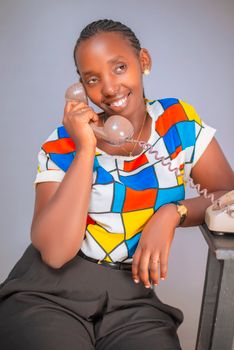 Smiling woman with vibrant shirt using a vintage rotary phone indoors.