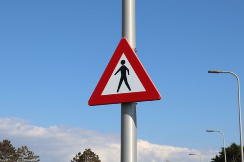 Free Pedestrian warning triangle traffic sign against a clear blue sky with lampposts. Stock Photo