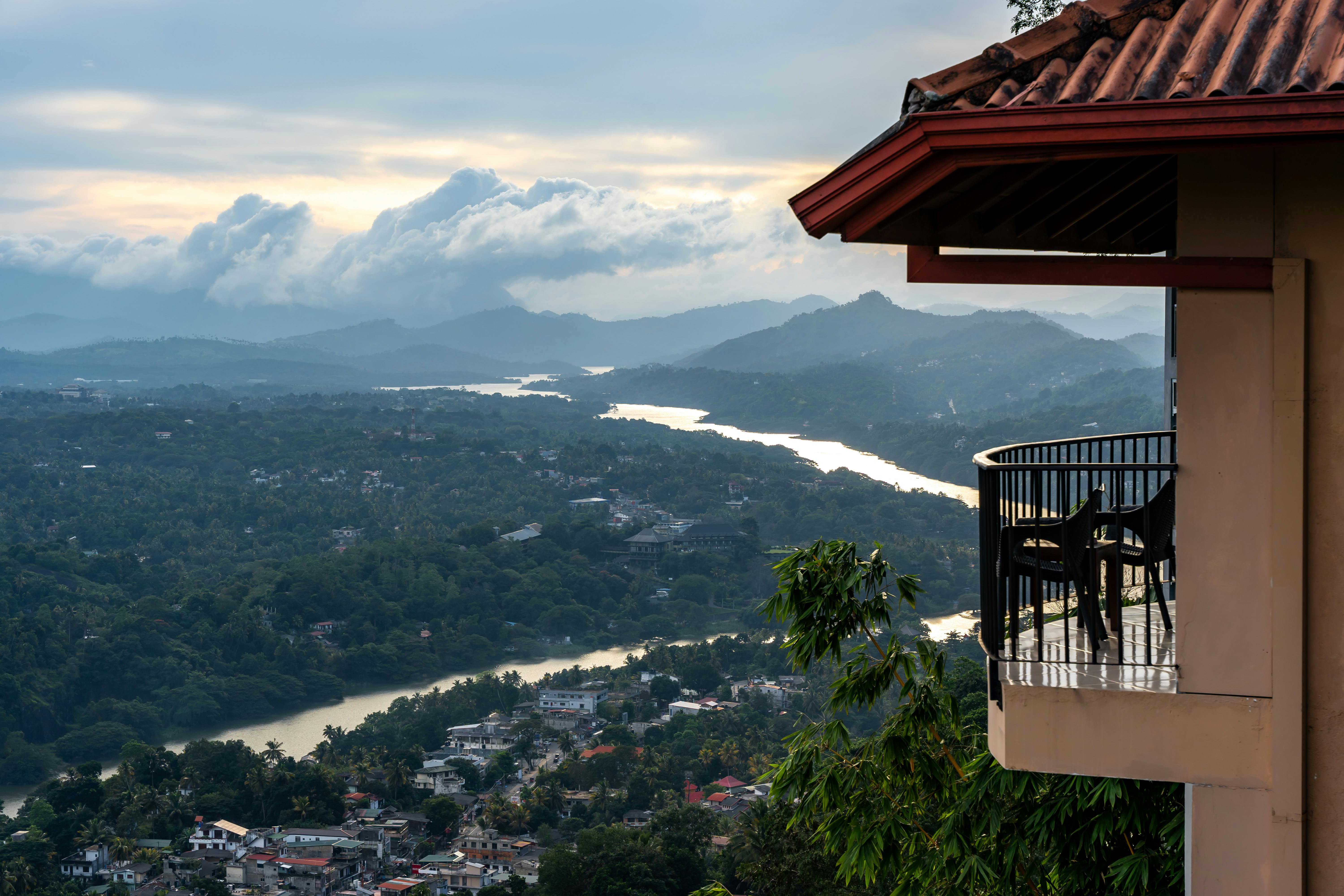 Picturesque view from a cozy balcony overlooking a lush valley and winding river at twilight. - ¿Dónde dormir en Kandy?