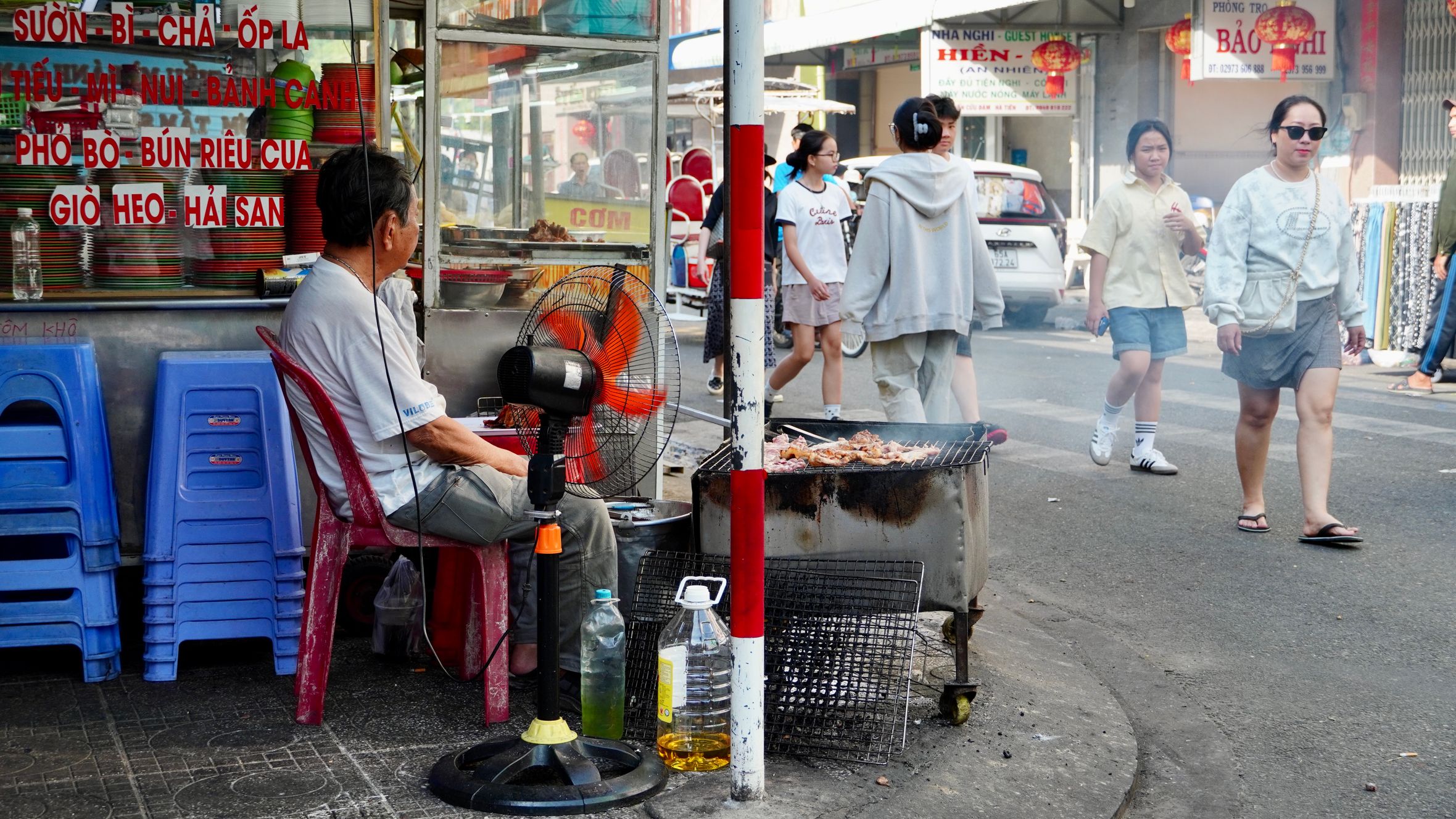 Grilling vendor at a bustling Ho Chi Minh City street with pedestrians.