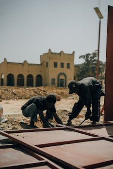 Two workers are installing a large panel at a construction site outdoors near an architectural building.