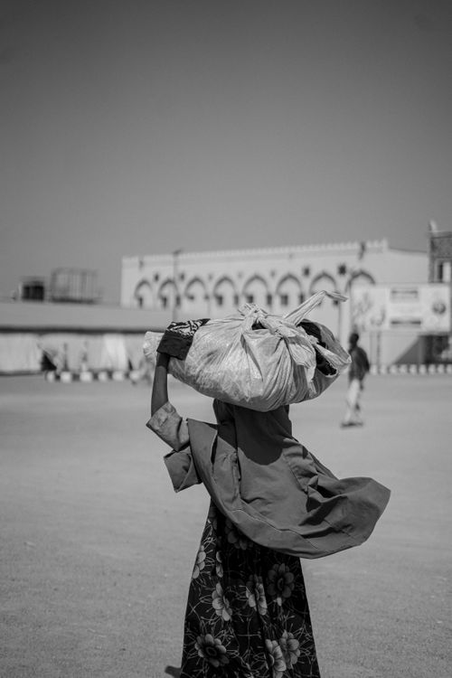 Free A woman carrying a large sack on her head in a public square in black and white. Stock Photo