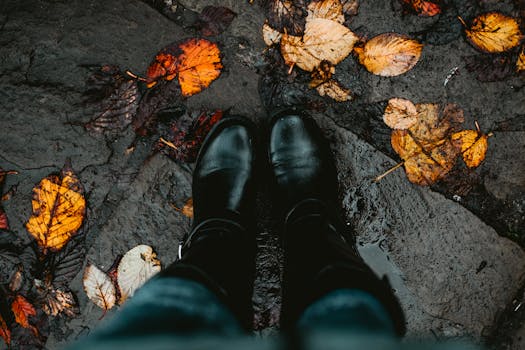 Two black boots on a leaf-covered, wet stone path, capturing the essence of autumn.