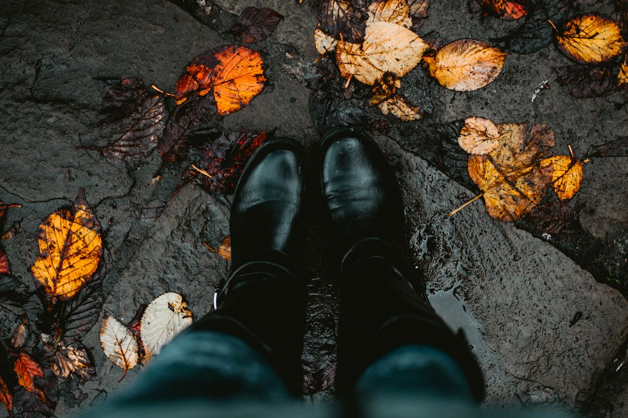 well-worn black boots on a wet leaf-covered stone path