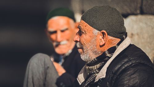 Free Two senior men wearing beanies sitting outdoors, bathed in warm sunlight. Stock Photo