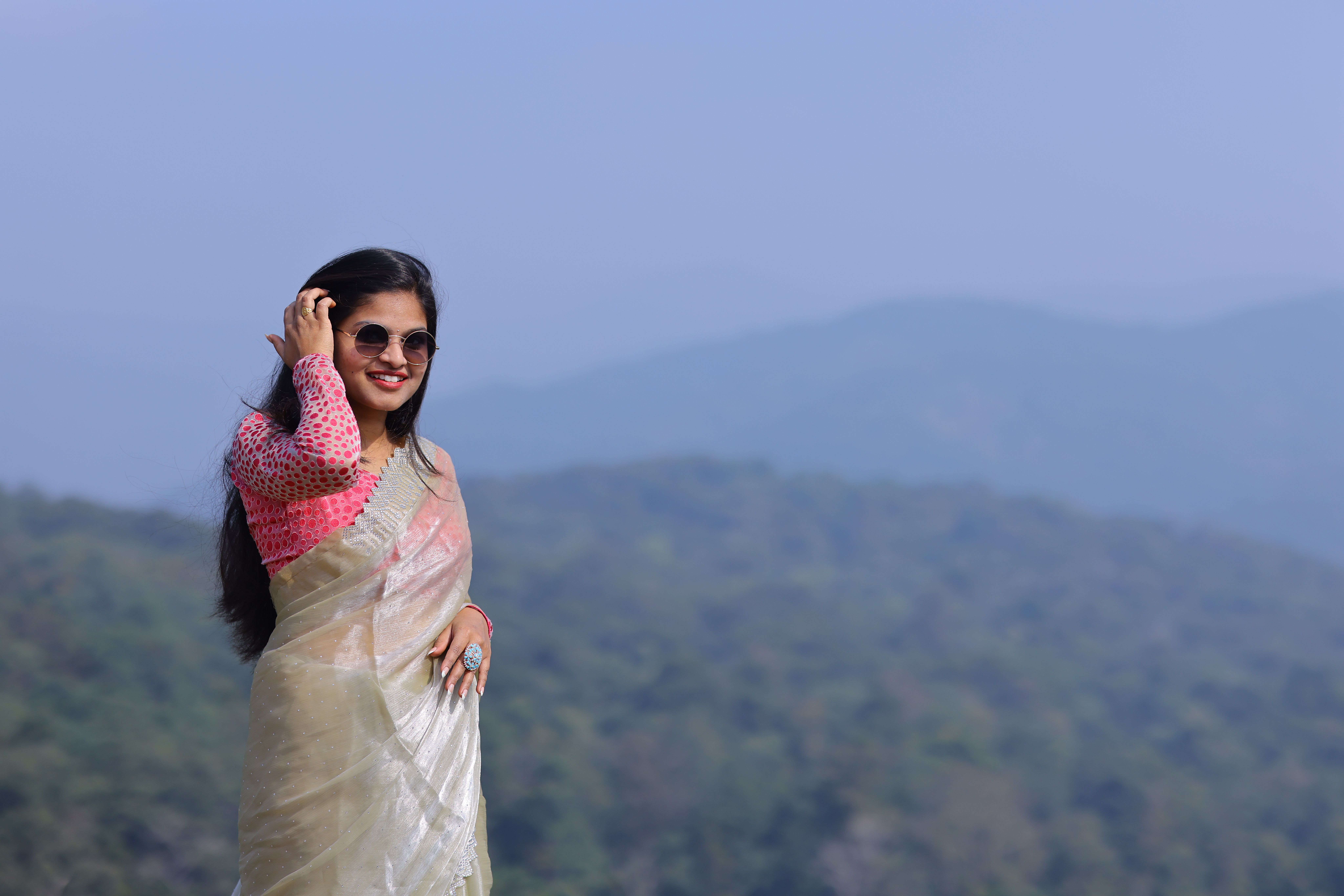 Gratis Kvinde i elegant sari smilende mod en naturskøn bjergrig baggrund på en solskinsdag. Lagerfoto