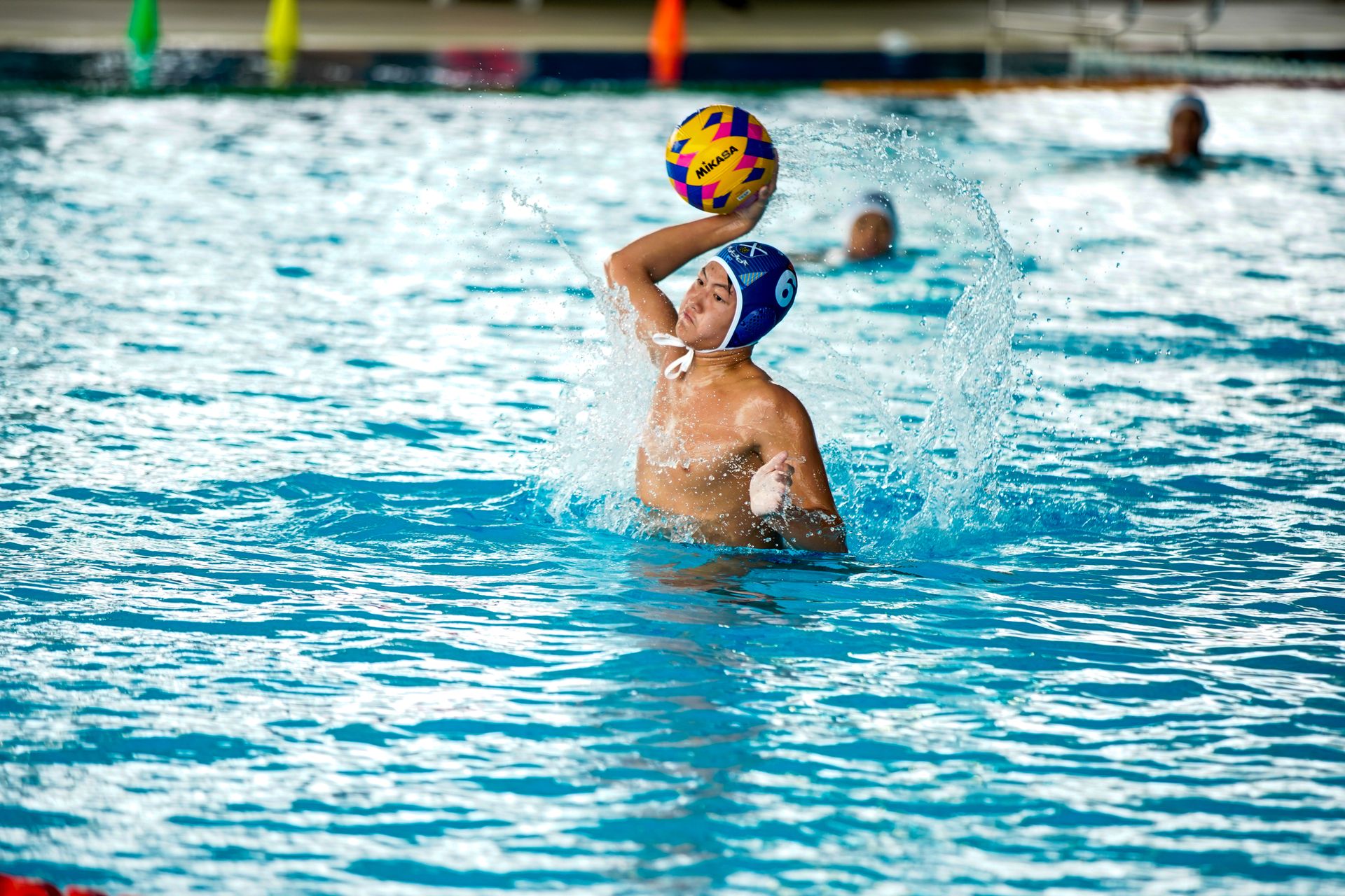Athlete in water polo match splashing in indoor pool setting.