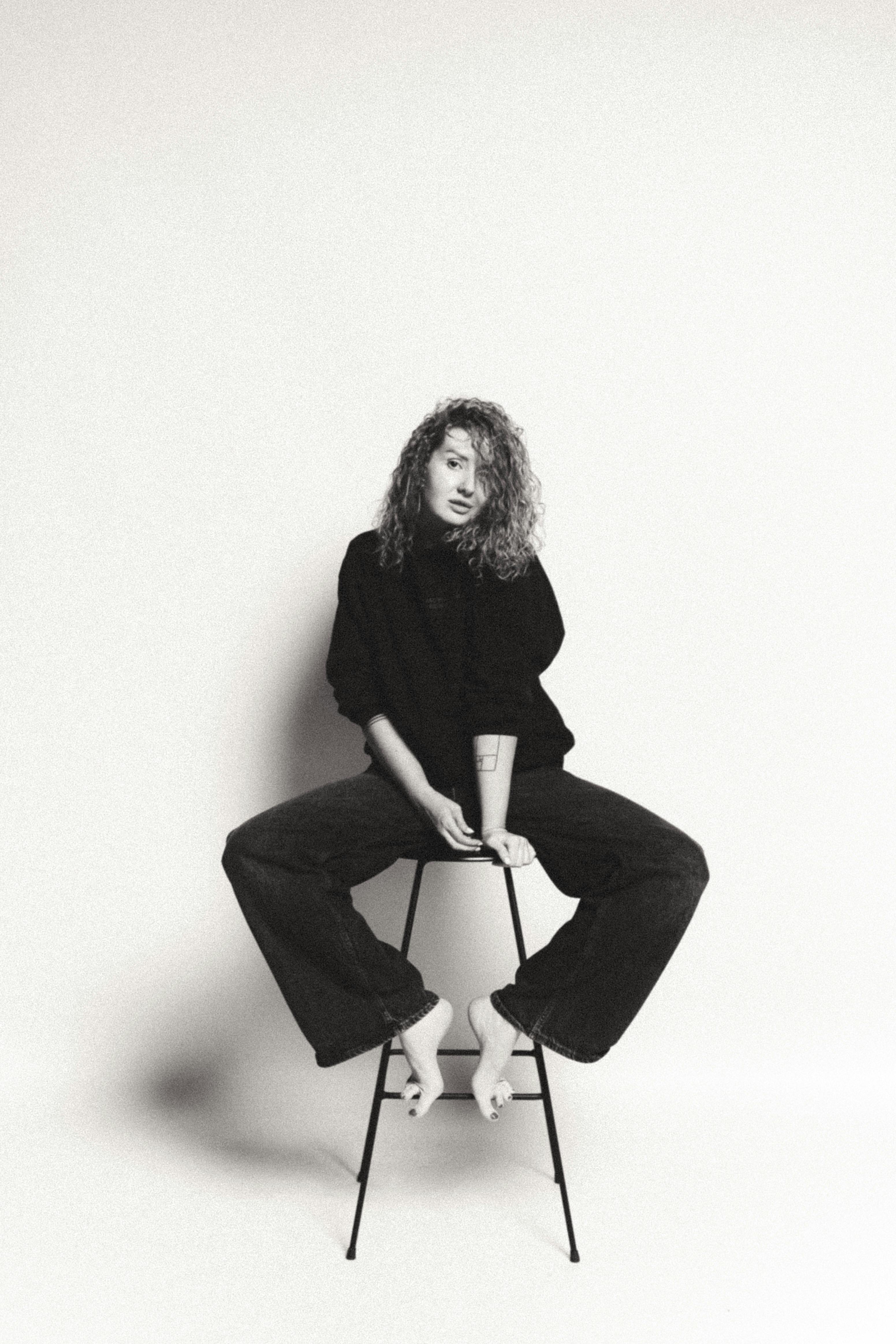 Artistic black and white portrait of a woman sitting on a stool, showcasing modern fashion.