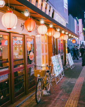 Night street scene with Japanese lanterns illuminating an alleyway, highlighting a bicycle and vibrant decor.