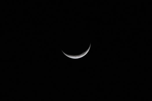 A sharp crescent moon glowing against a dark, starless night sky.