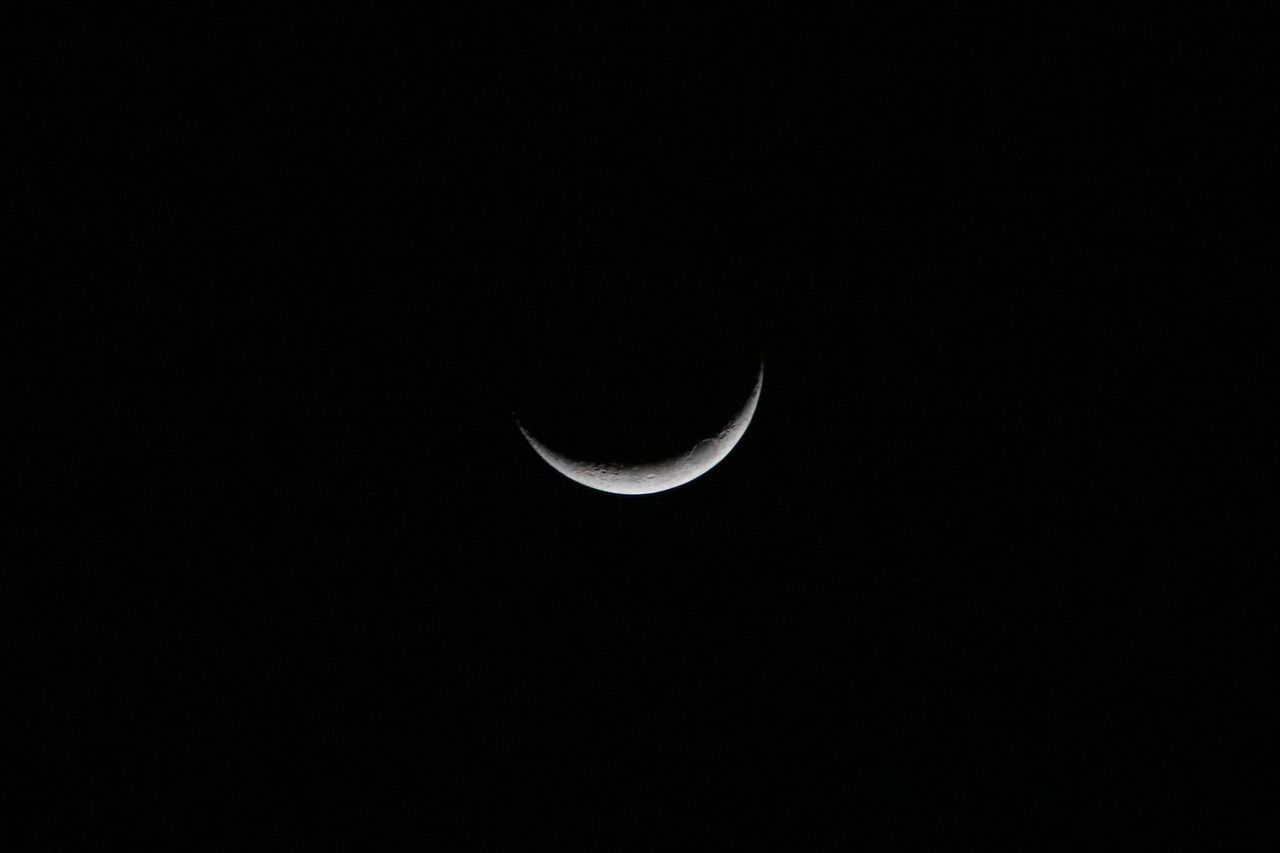 a sharp crescent moon glowing against a dark starless night sky