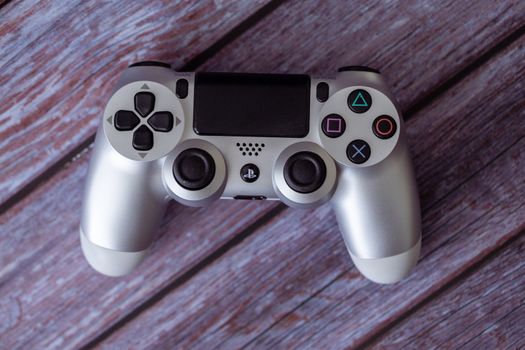 Top view of a silver PlayStation controller on a rustic wooden background.