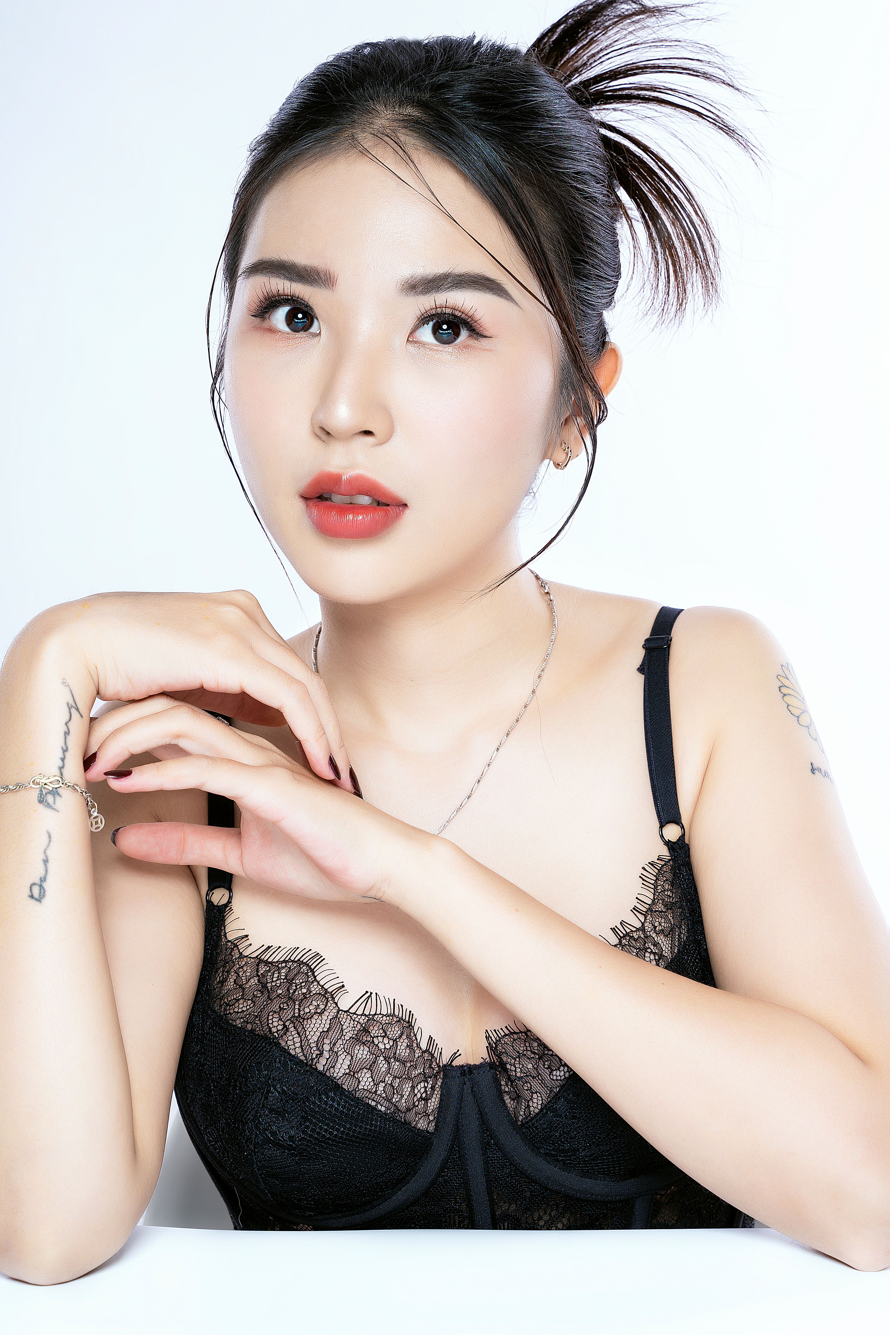 Close-up portrait of a young woman with tattoos and stylish makeup posing elegantly against a white background.