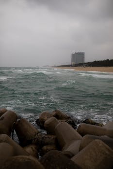 A moody seaside scene with crashing waves and concrete breakwaters under an overcast sky.