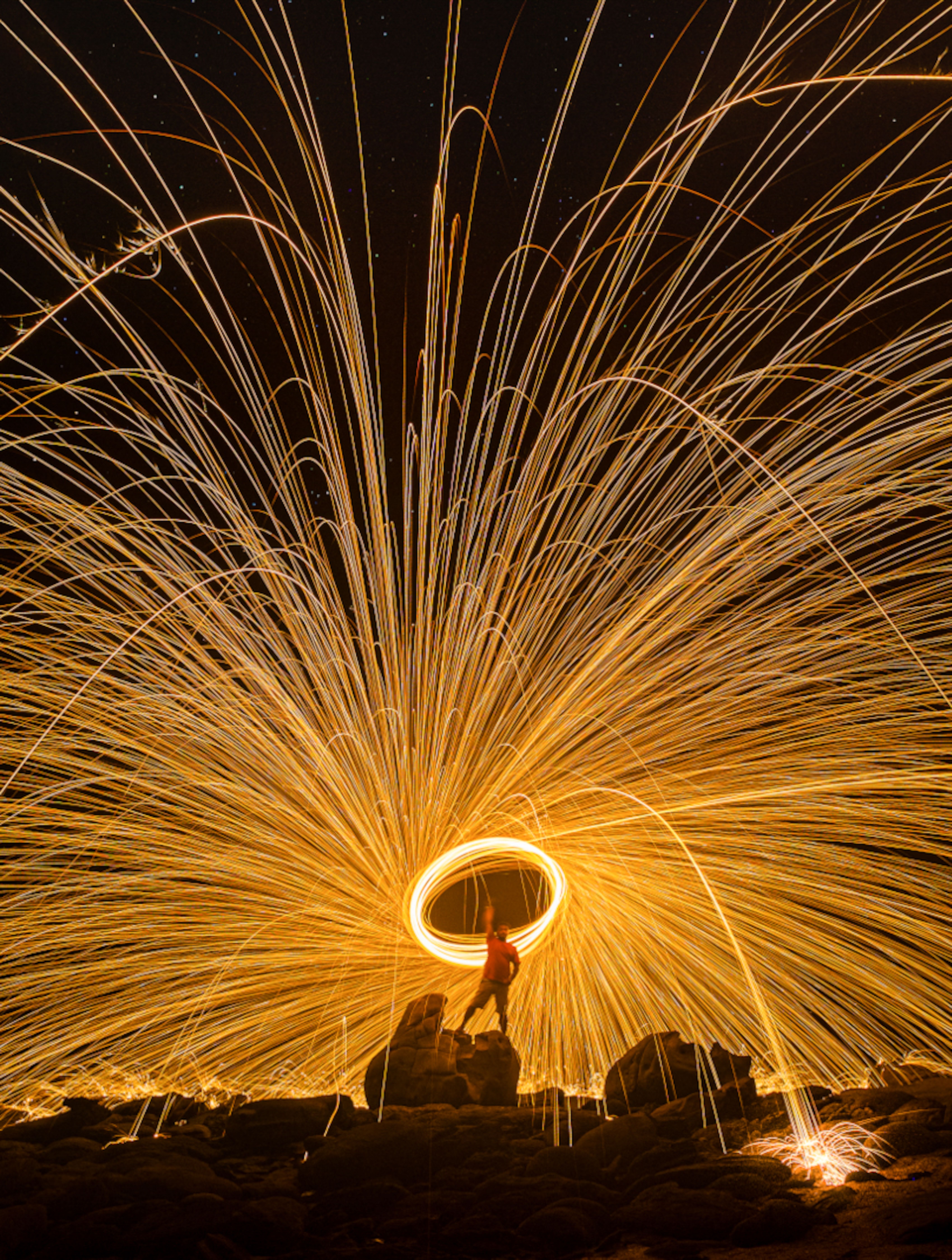 Fotomural Deslumbrante fotografía nocturna de larga exposición de fuego giratorio que crea estelas de luz sobre terreno rocoso.