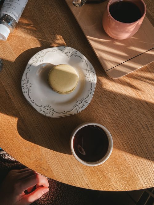 Free Enjoy a peaceful afternoon tea with a macaron on a sunlit wooden table, perfect for a cozy break. Stock Photo