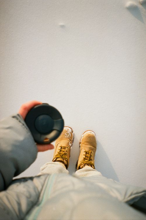 Free Person holding coffee cup outdoors in snow wearing yellow boots and winter coat. Stock Photo