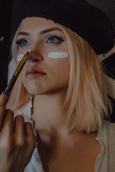 Close-up portrait of a woman in a beret with paintbrush and artistic makeup.