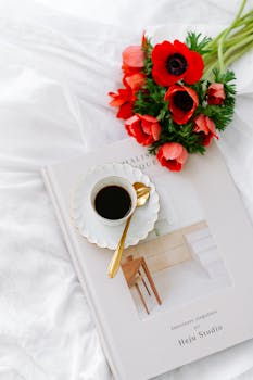 A cup of coffee and red flowers elegantly placed on a design book, creating a cozy aesthetic.