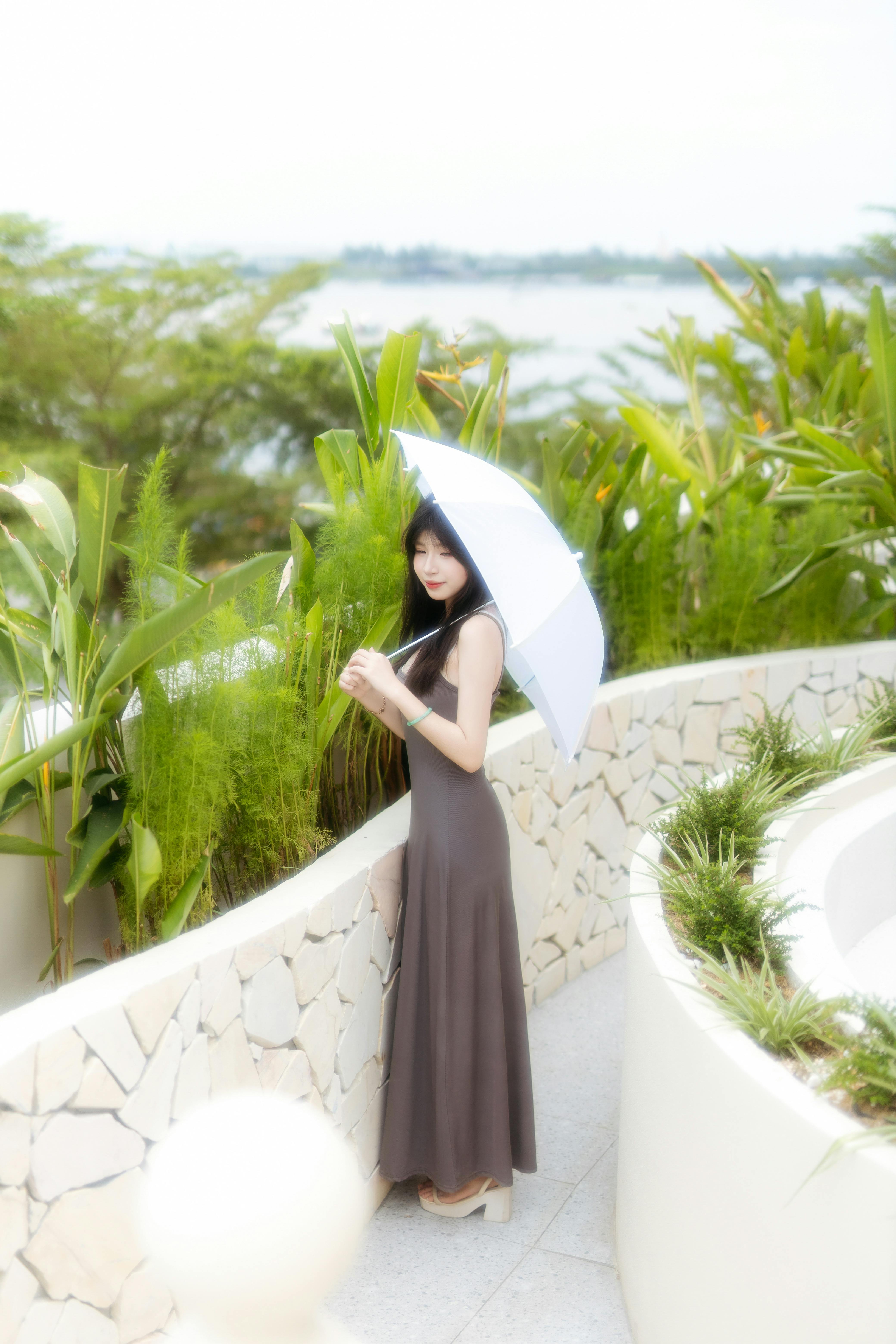 Woman standing with umbrella in lush tropical garden on a sunny day.