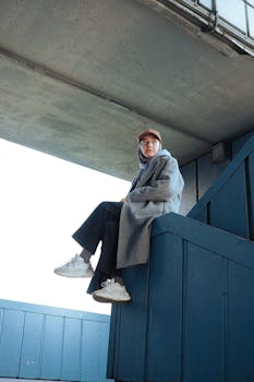 Person sitting on urban blue structure, dressed in casual modern attire and neutral colors.