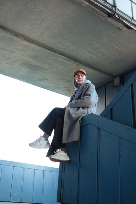 Person sitting on urban blue structure, dressed in casual modern attire and neutral colors.