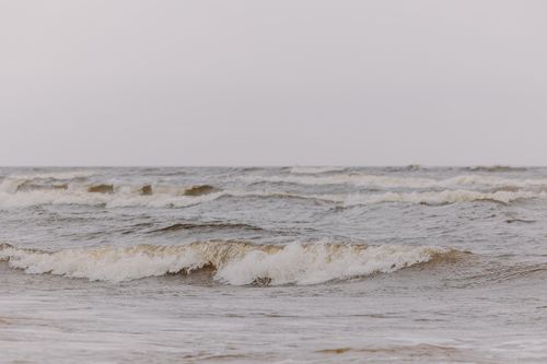 Free Peaceful waves gently rolling onto a serene beach with a muted sky above. Stock Photo