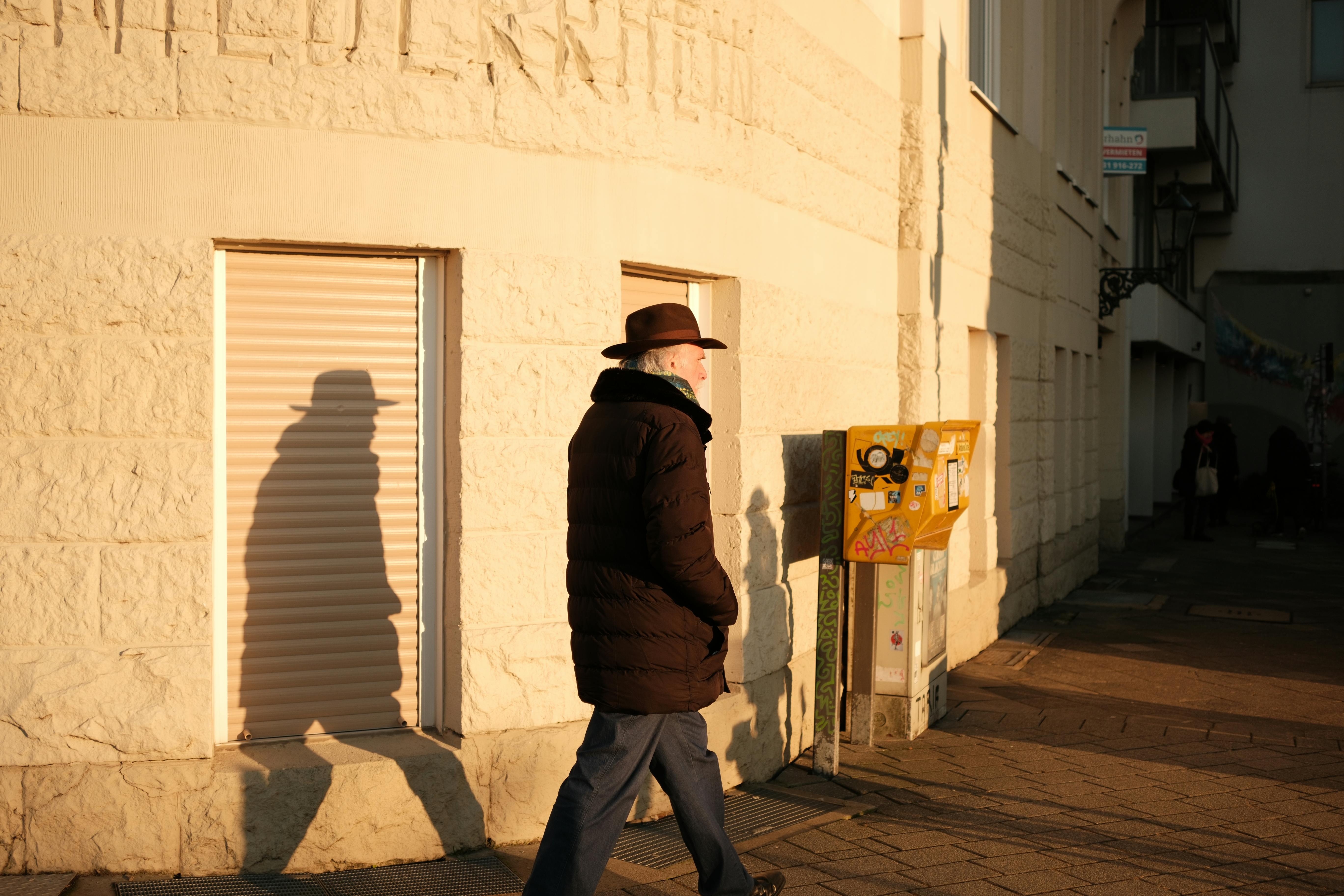 Man in a hat walking past a sunlit building in Düsseldorf, Germany.