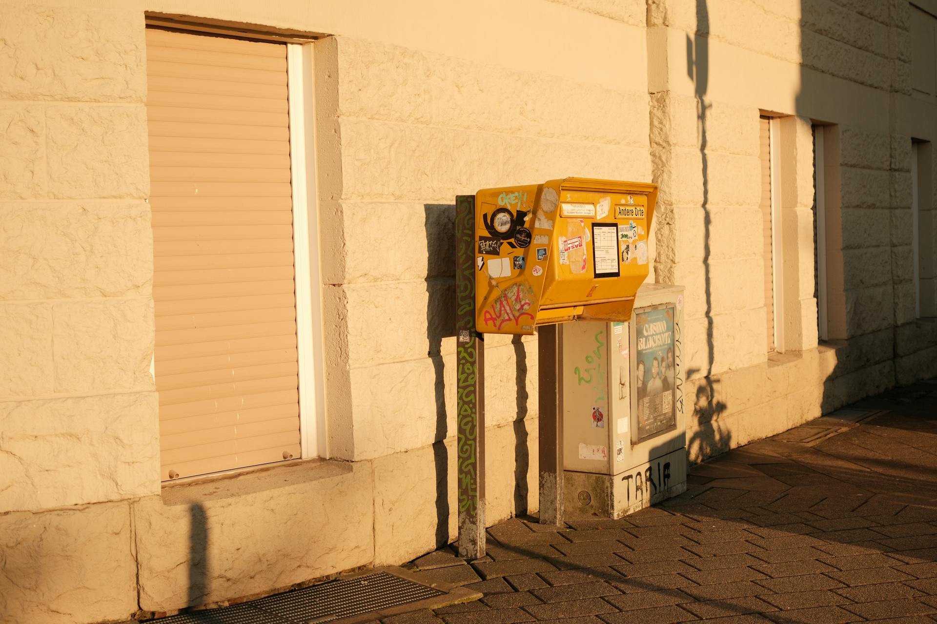 Yellow mailbox against a sunlit building wall in Düsseldorf, Germany.