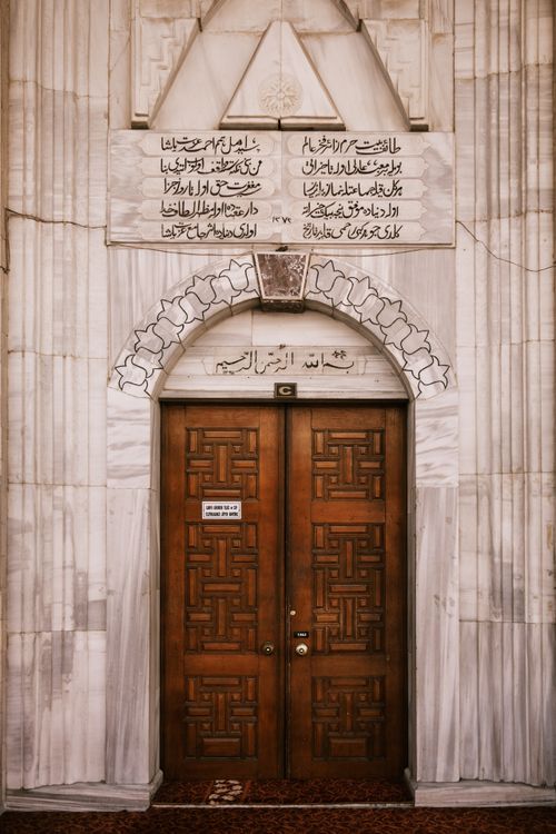 Free Beautifully carved wooden door with intricate Arabic inscriptions on a stone facade. Stock Photo
