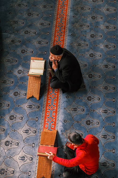 Free Two people in traditional attire reading in a mosque interior setting. Stock Photo
