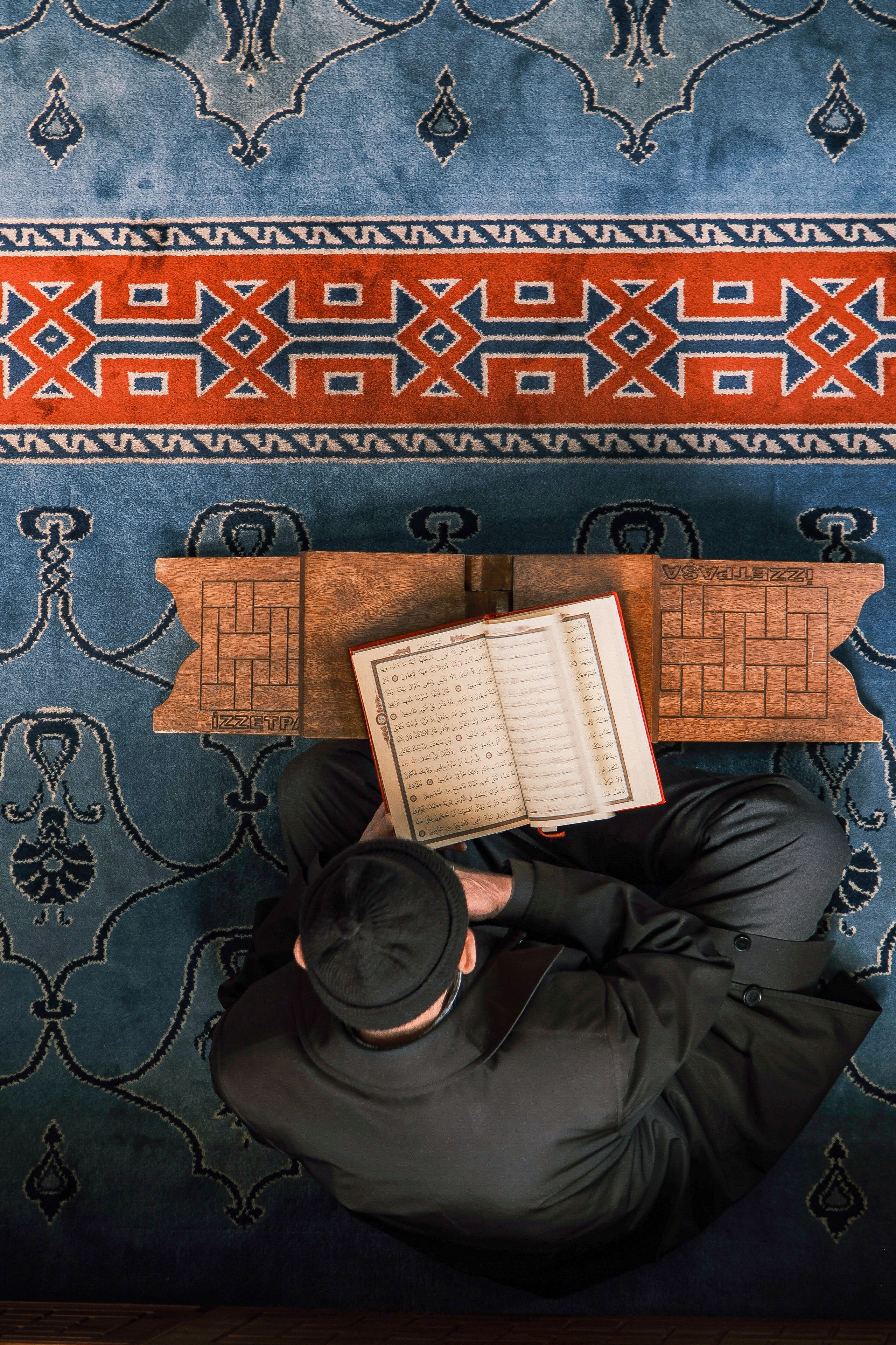 Man Reading Religious Text on Decorative Carpet · Free Stock Photo